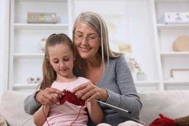 Photo of Smiling grandmother teaching her granddaughter to knit at home