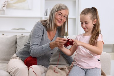 Grandmother teaching her granddaughter to knit on sofa at home