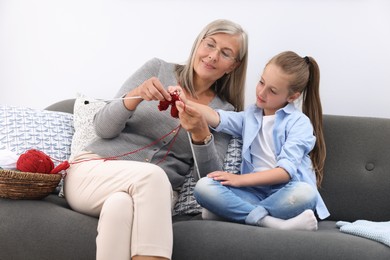 Grandmother teaching her granddaughter to knit on sofa at home