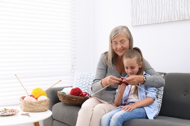 Photo of Smiling grandmother teaching her granddaughter to knit on sofa at home. Space for text