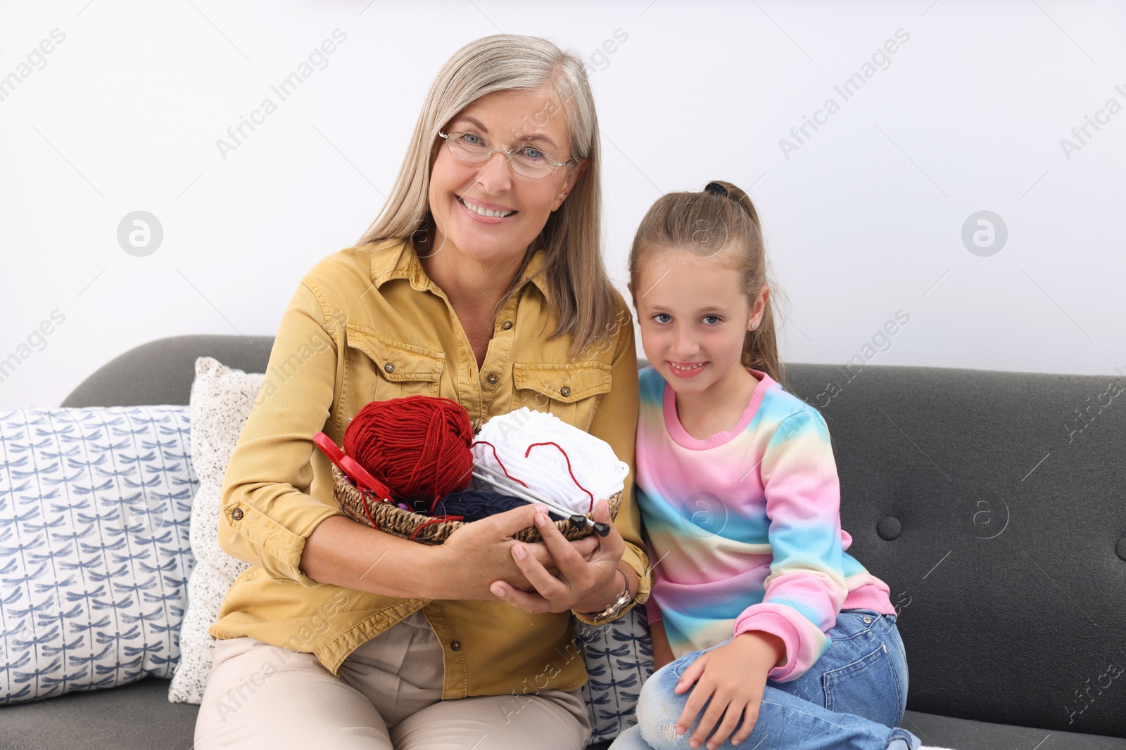 Photo of Happy grandmother and granddaughter with skeins of yarn on sofa at home