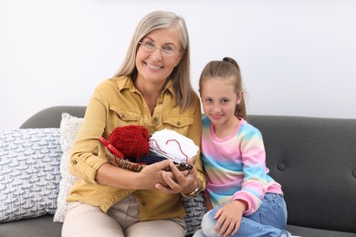 Happy grandmother and granddaughter with skeins of yarn on sofa at home