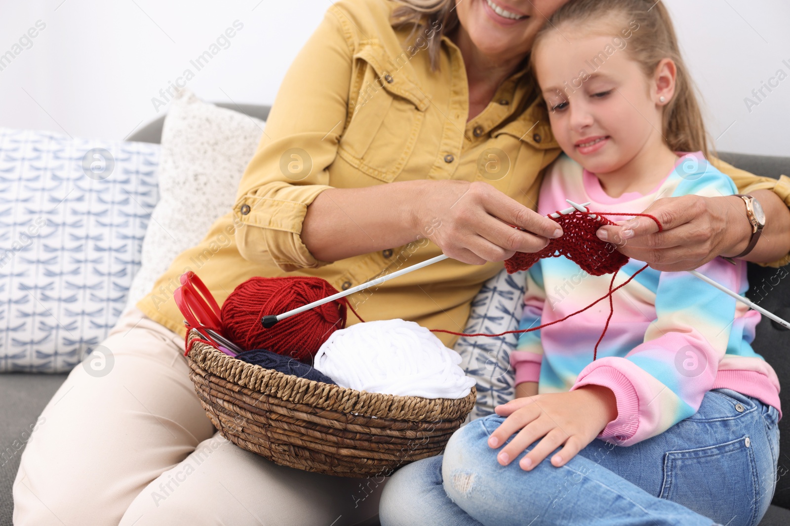 Photo of Smiling grandmother teaching her granddaughter to knit at home, closeup