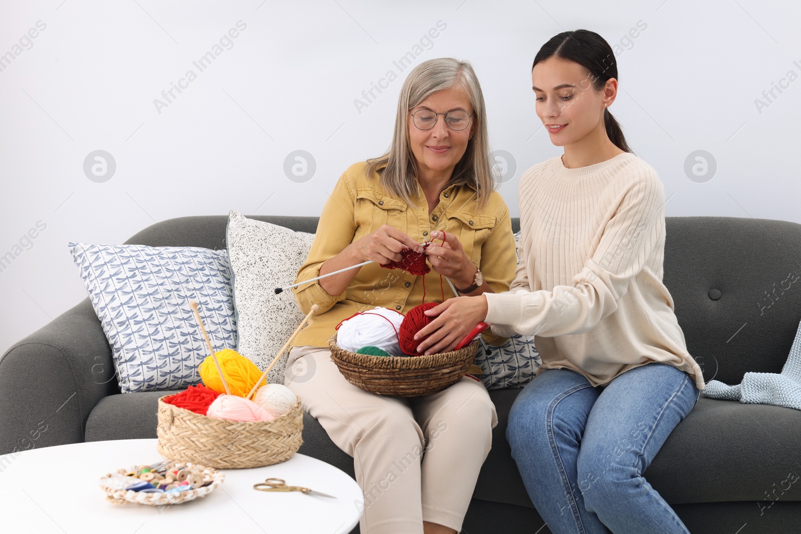 Photo of Daughter observing how her mother knitting on sofa at home