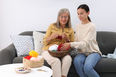 Daughter observing how her mother knitting on sofa at home