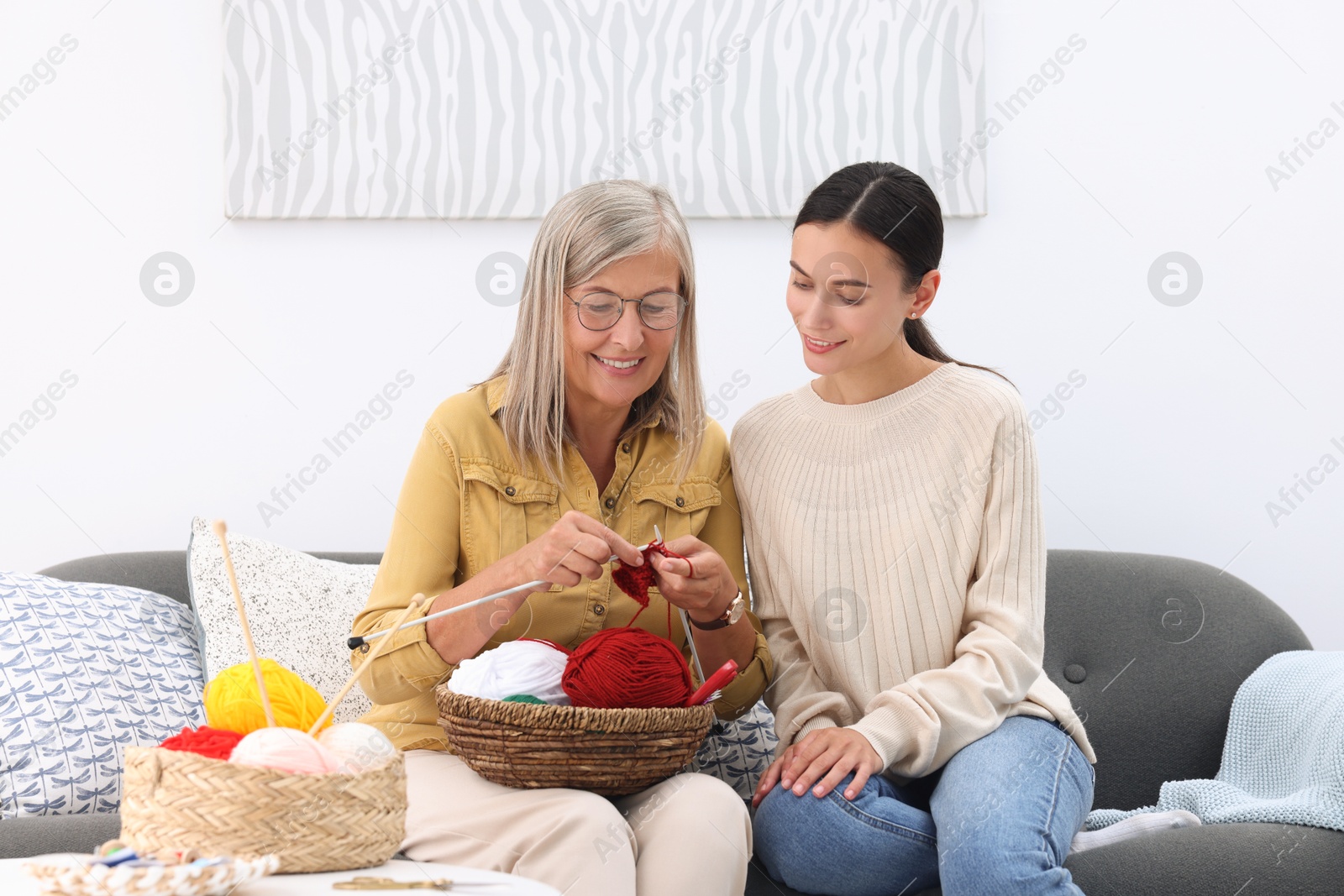 Photo of Smiling daughter observing her mother knitting on sofa at home