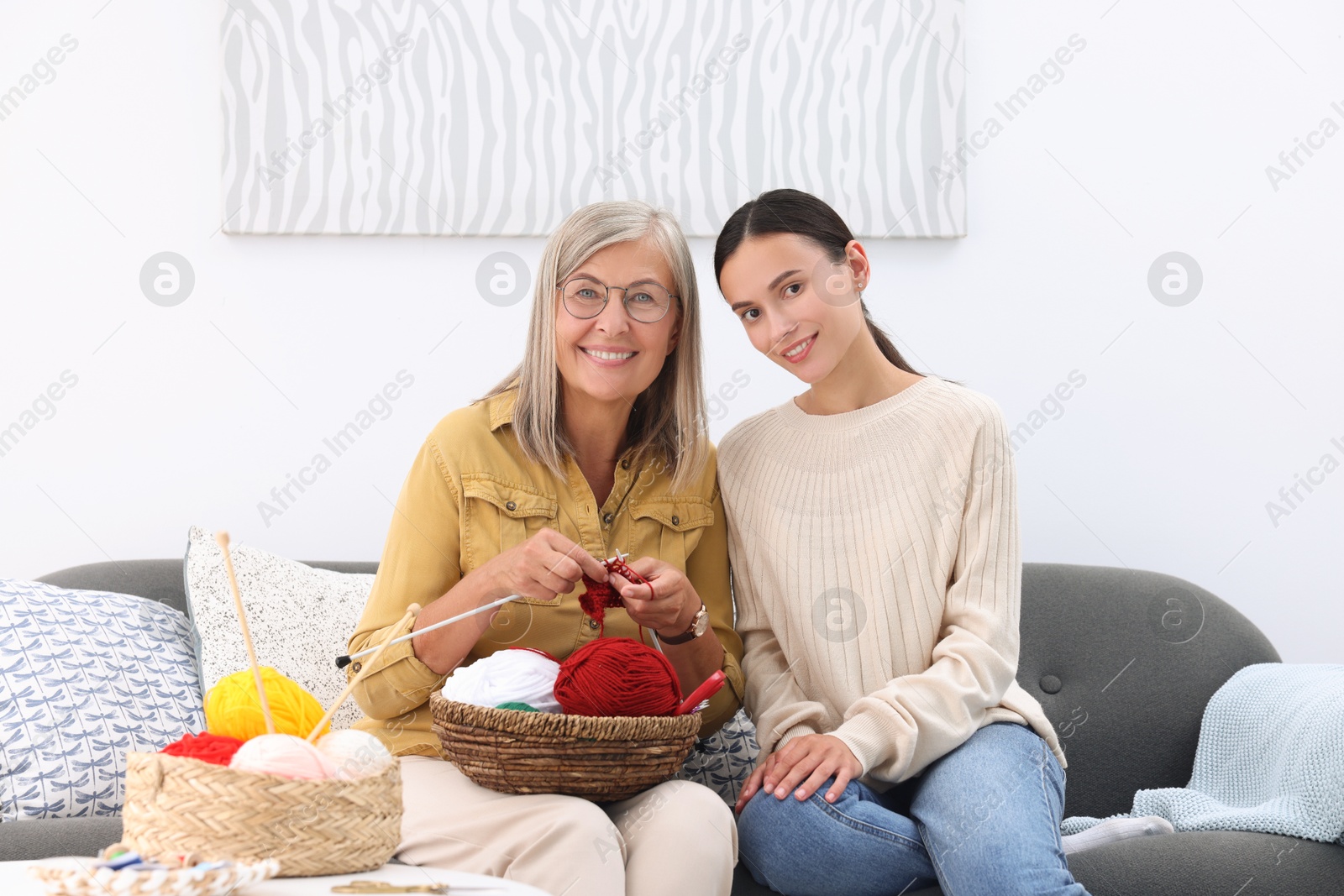 Photo of Happy mother and daughter with skeins of yarn on sofa at home