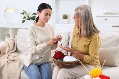 Photo of Mother observing her daughter knitting on sofa at home