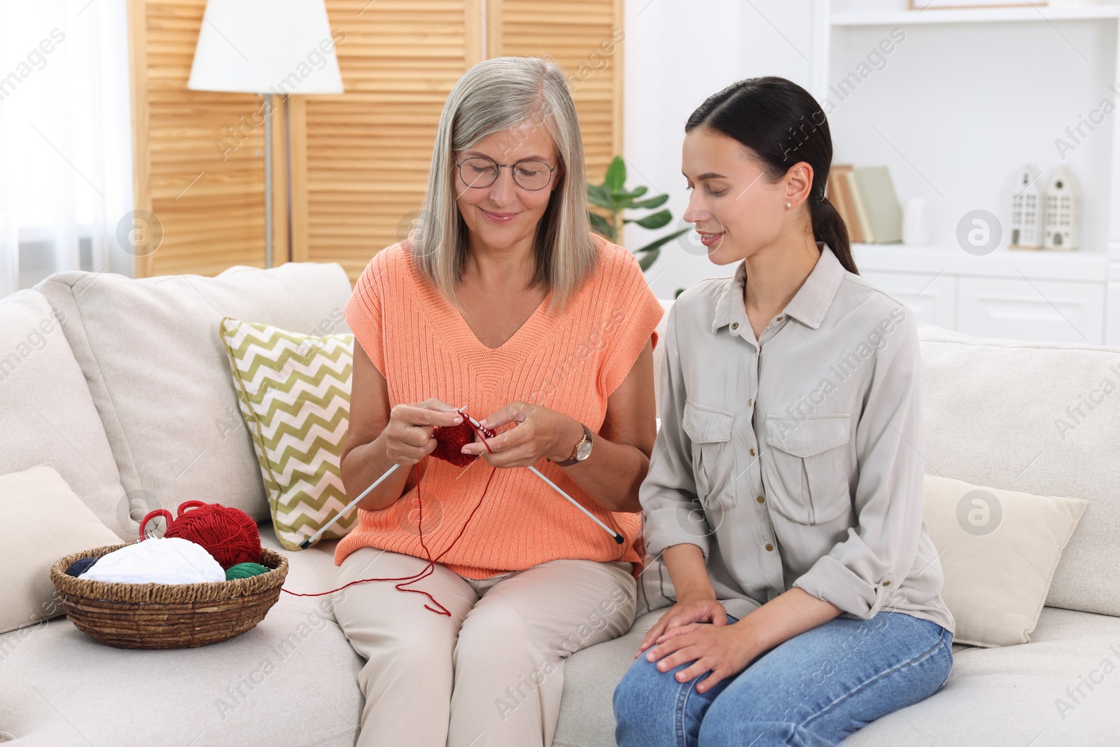 Photo of Smiling daughter observing her mother knitting on sofa at home