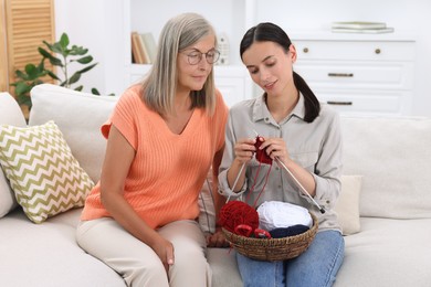 Mother observing her daughter knitting on sofa at home