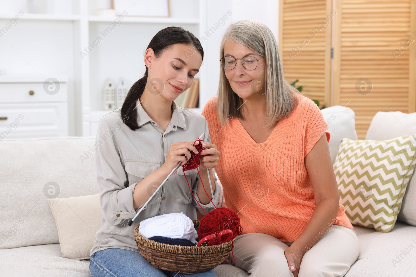 Photo of Mother observing her daughter knitting on sofa at home