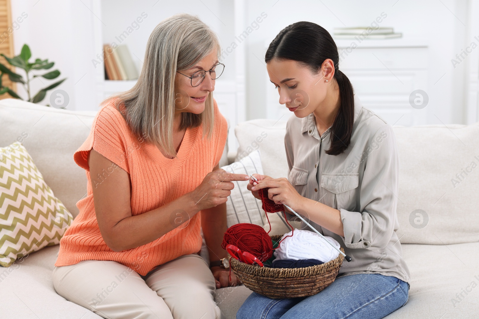 Photo of Mother teaching her daughter how to knit on sofa at home