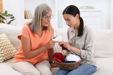 Mother teaching her daughter how to knit on sofa at home