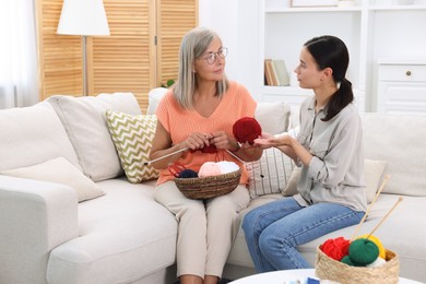 Daughter talking to her mother while she knitting on sofa at home