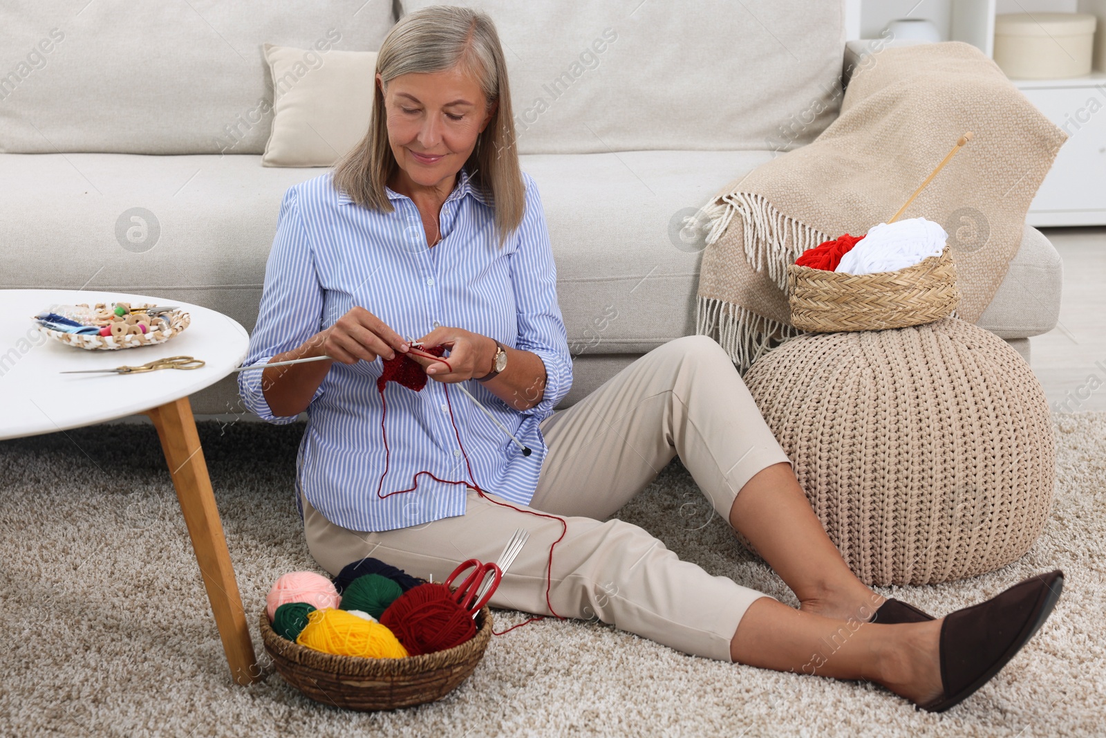 Photo of Beautiful senior woman knitting near sofa at home