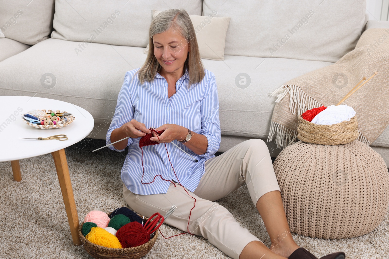 Photo of Smiling senior woman knitting near sofa at home