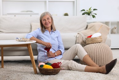 Smiling woman with skeins of yarn near sofa at home