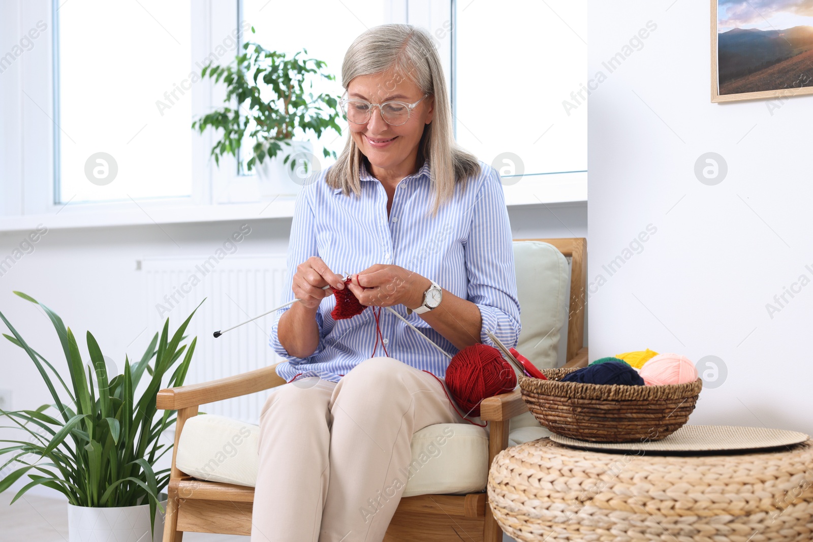 Photo of Smiling senior woman knitting on armchair at home