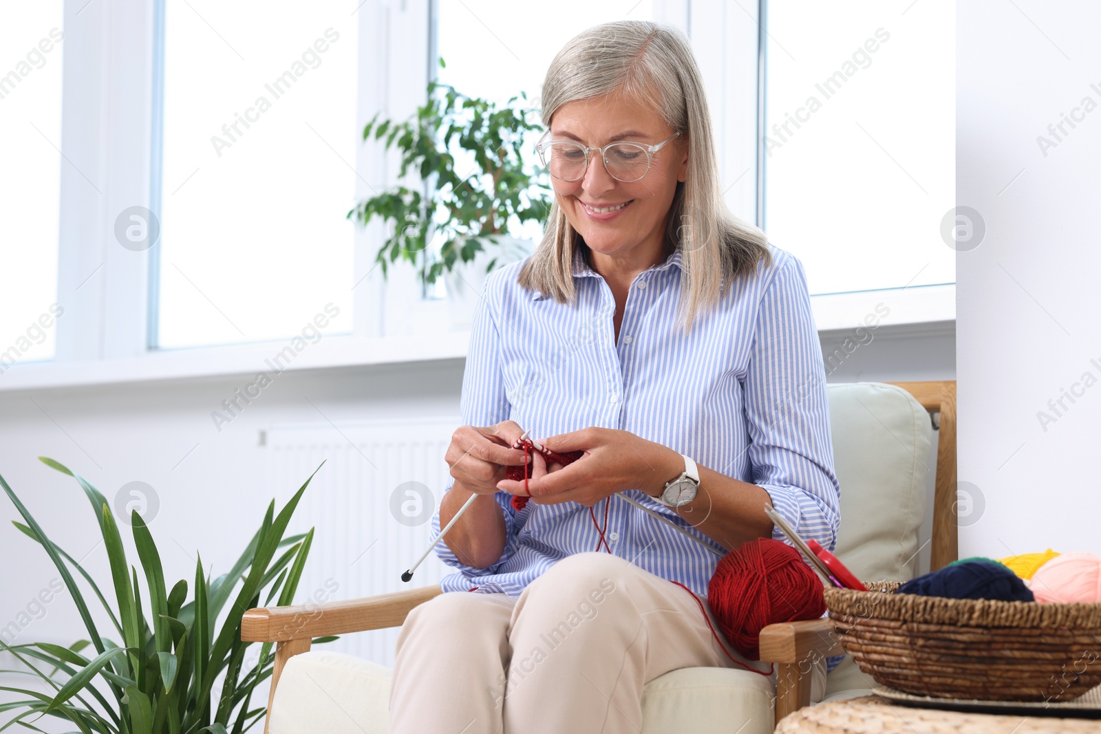 Photo of Smiling senior woman knitting on armchair at home