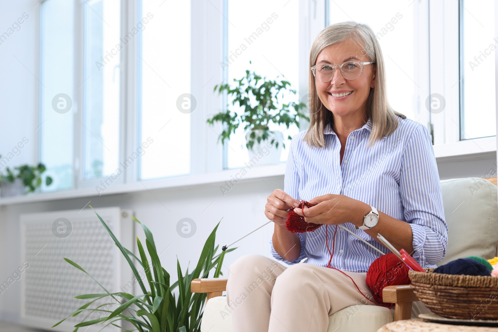 Photo of Smiling woman knitting on armchair at home. Space for text