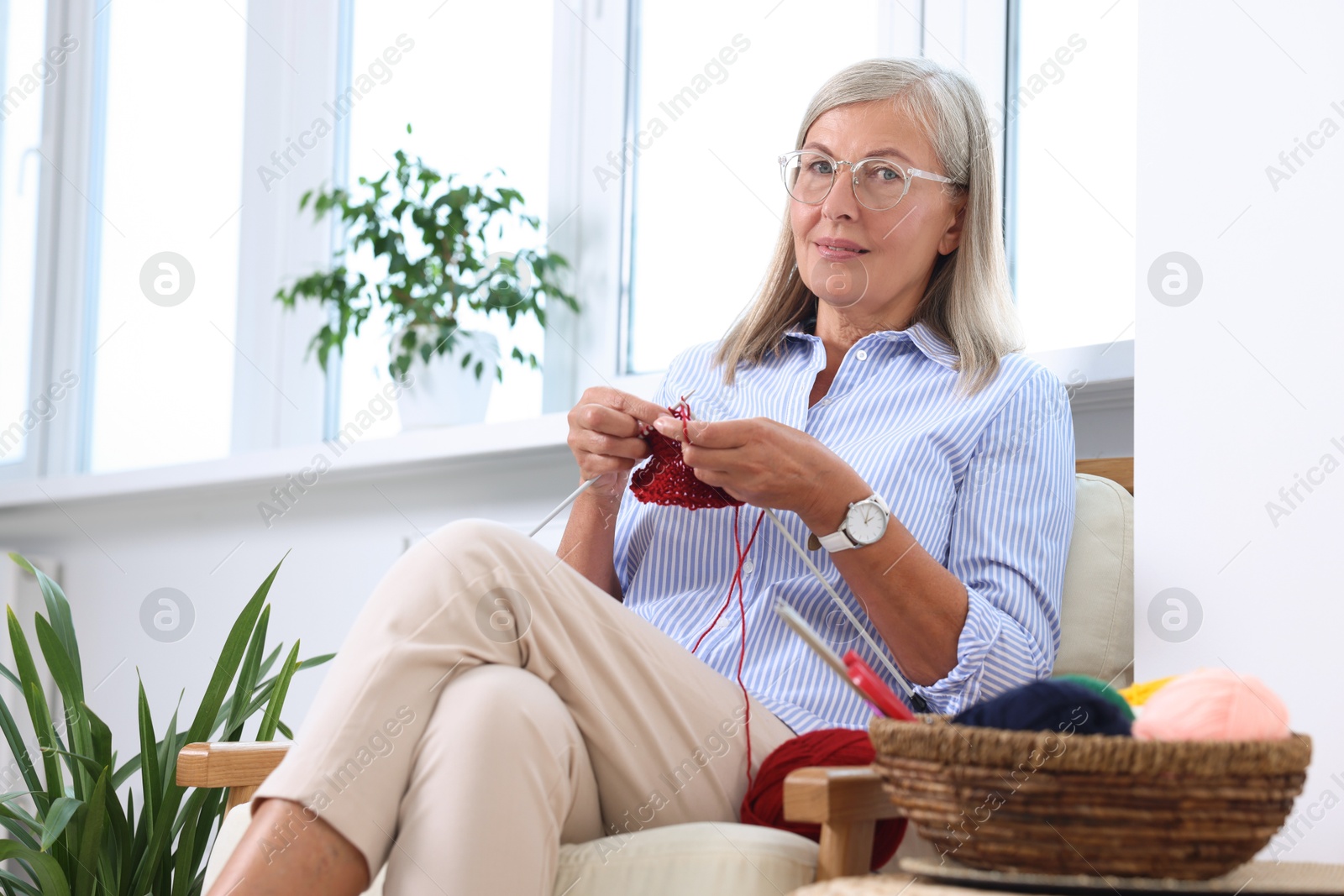 Photo of Beautiful woman knitting on armchair at home, low angle view