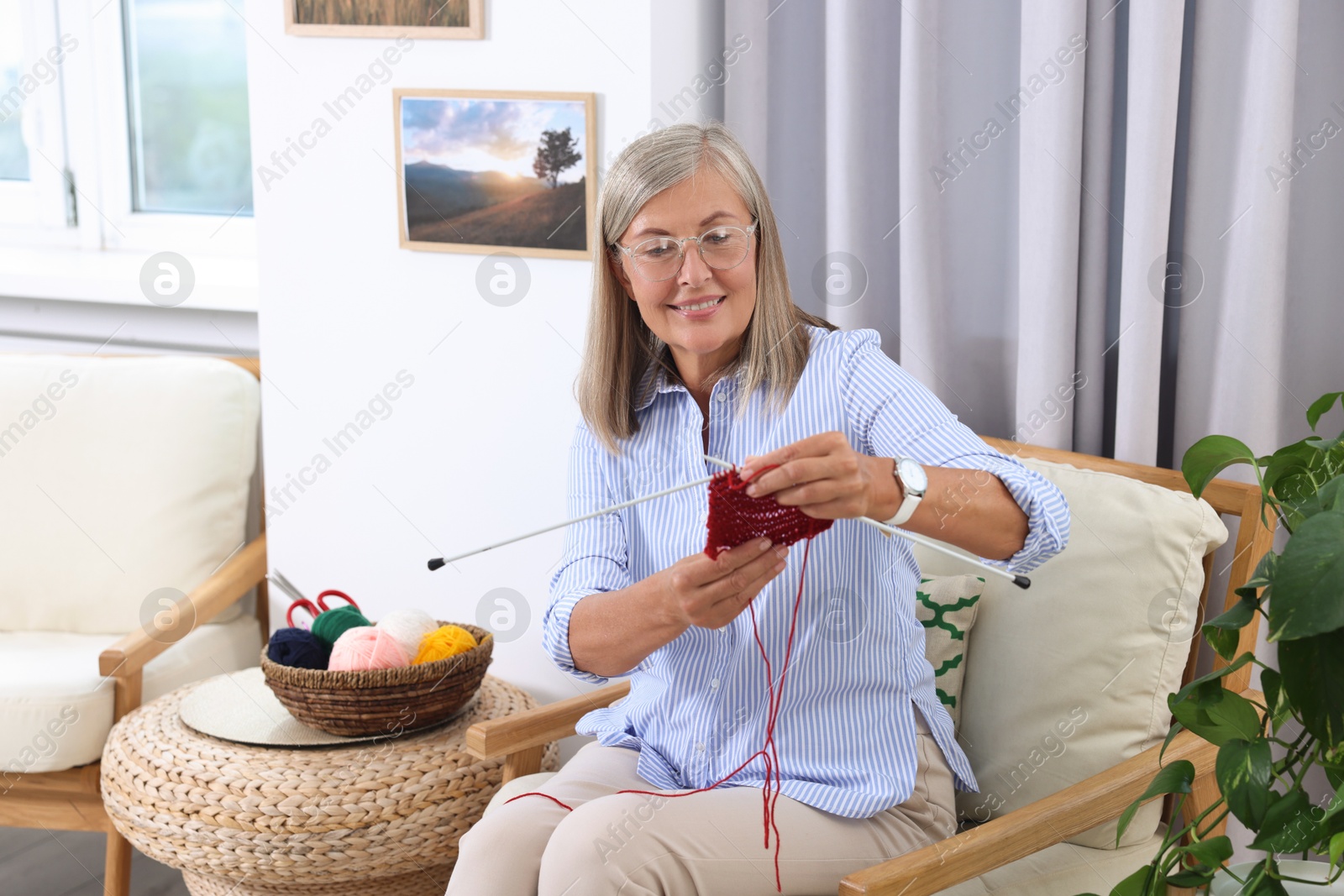 Photo of Smiling senior woman knitting on armchair at home