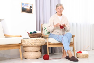 Photo of Beautiful senior woman knitting on armchair at home