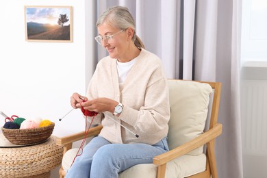 Photo of Smiling senior woman knitting on armchair at home