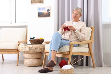 Beautiful senior woman knitting on armchair at home