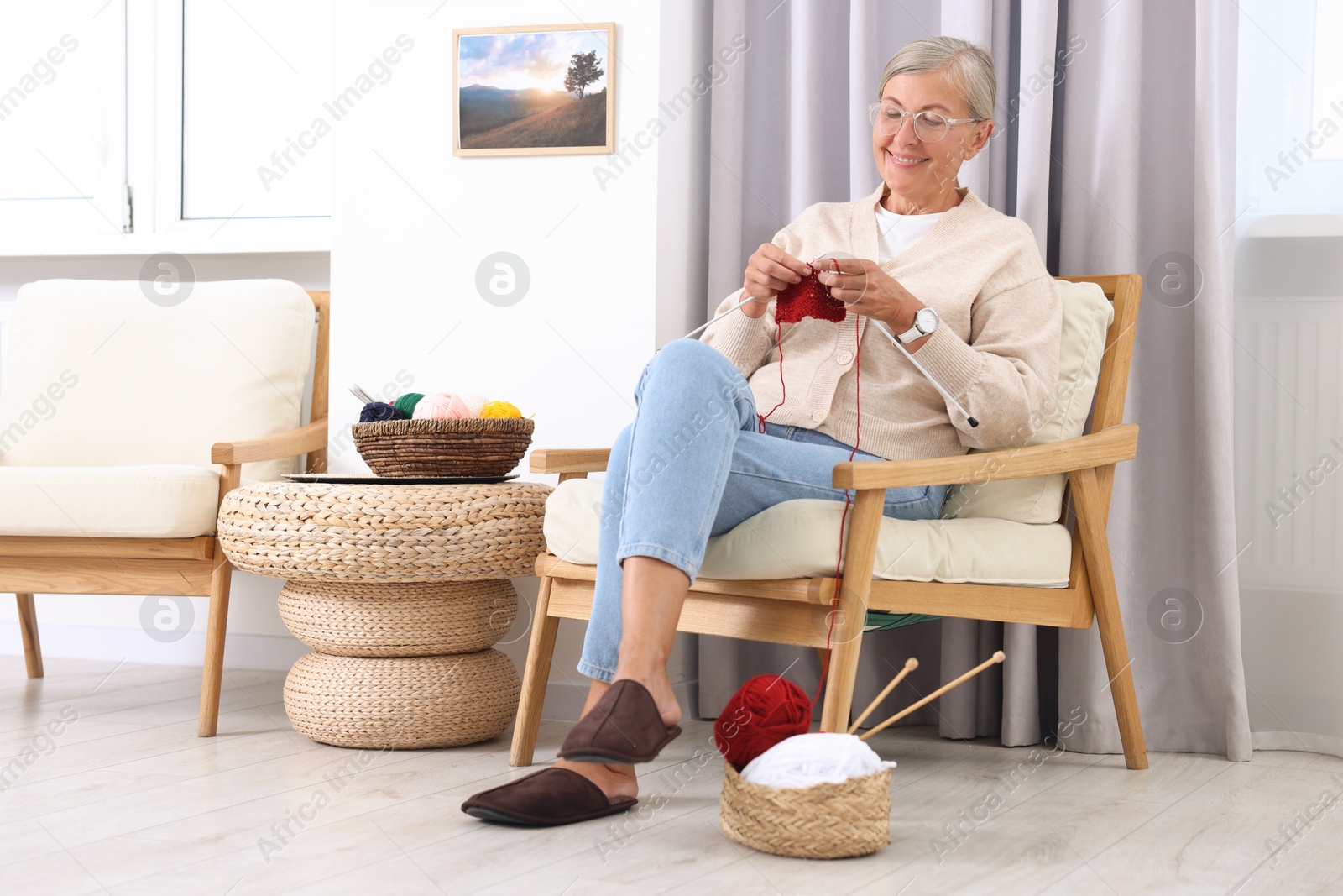 Photo of Smiling senior woman knitting on armchair at home