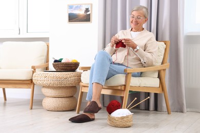 Smiling senior woman knitting on armchair at home