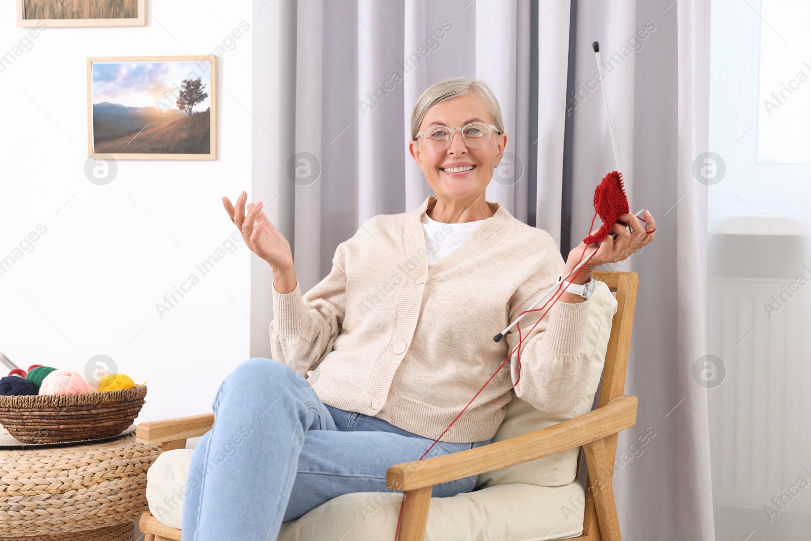 Photo of Smiling woman with knitting needles sitting on armchair at home