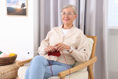 Photo of Beautiful senior woman knitting on armchair at home