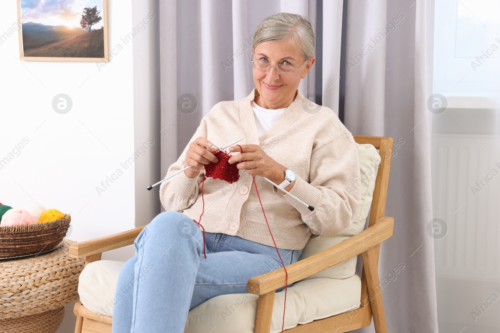 Photo of Beautiful senior woman knitting on armchair at home