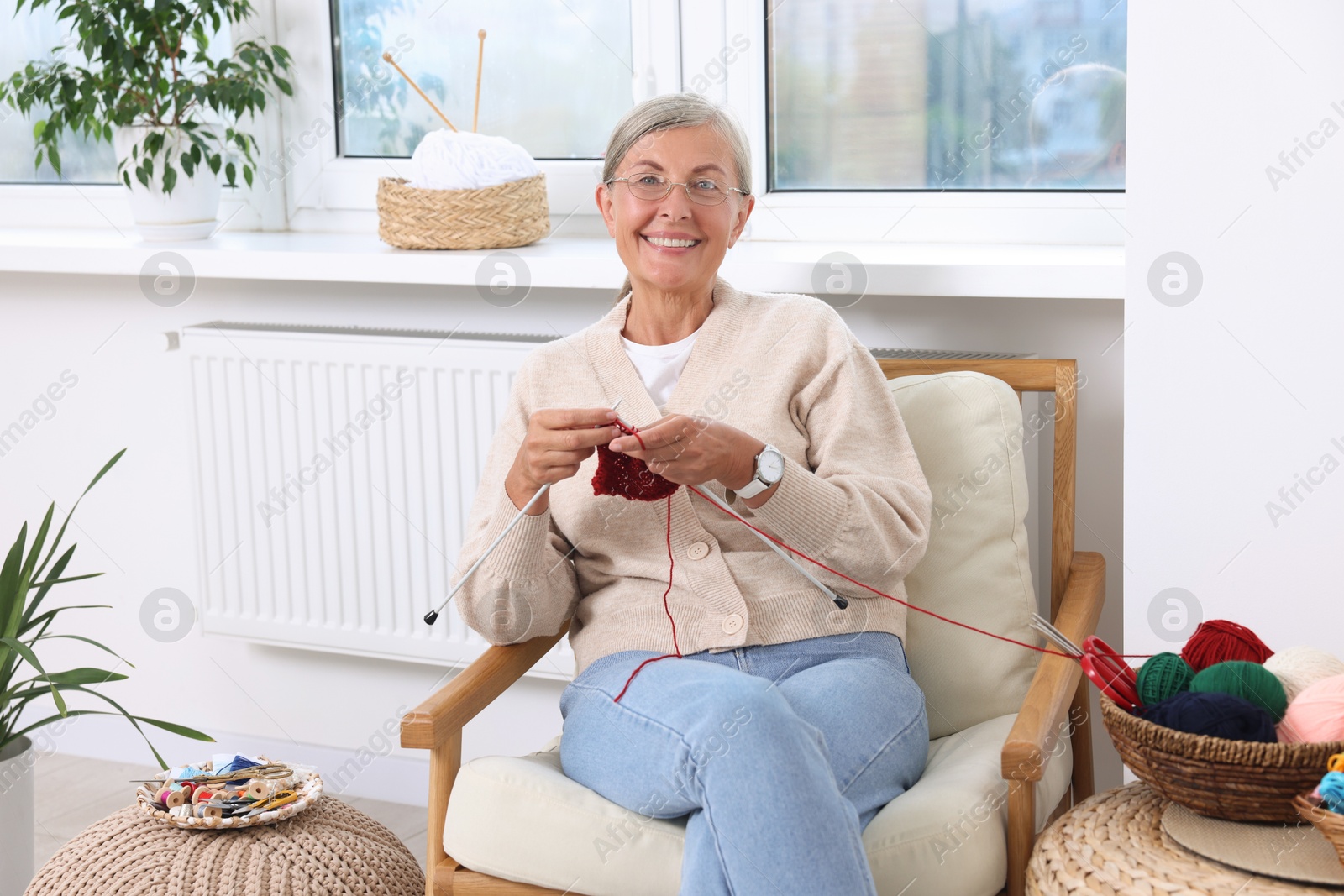 Photo of Smiling senior woman knitting on armchair at home