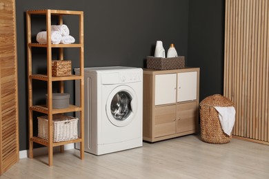 Photo of Washing machine, detergents in basket, wooden rack and storage cabinet indoors