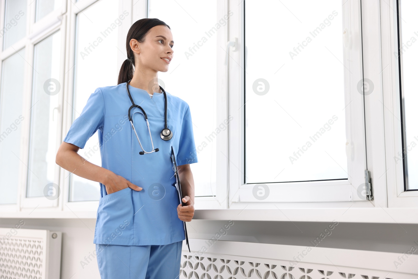 Photo of Smiling nurse with clipboard near window in clinic, low angle view. Space for text