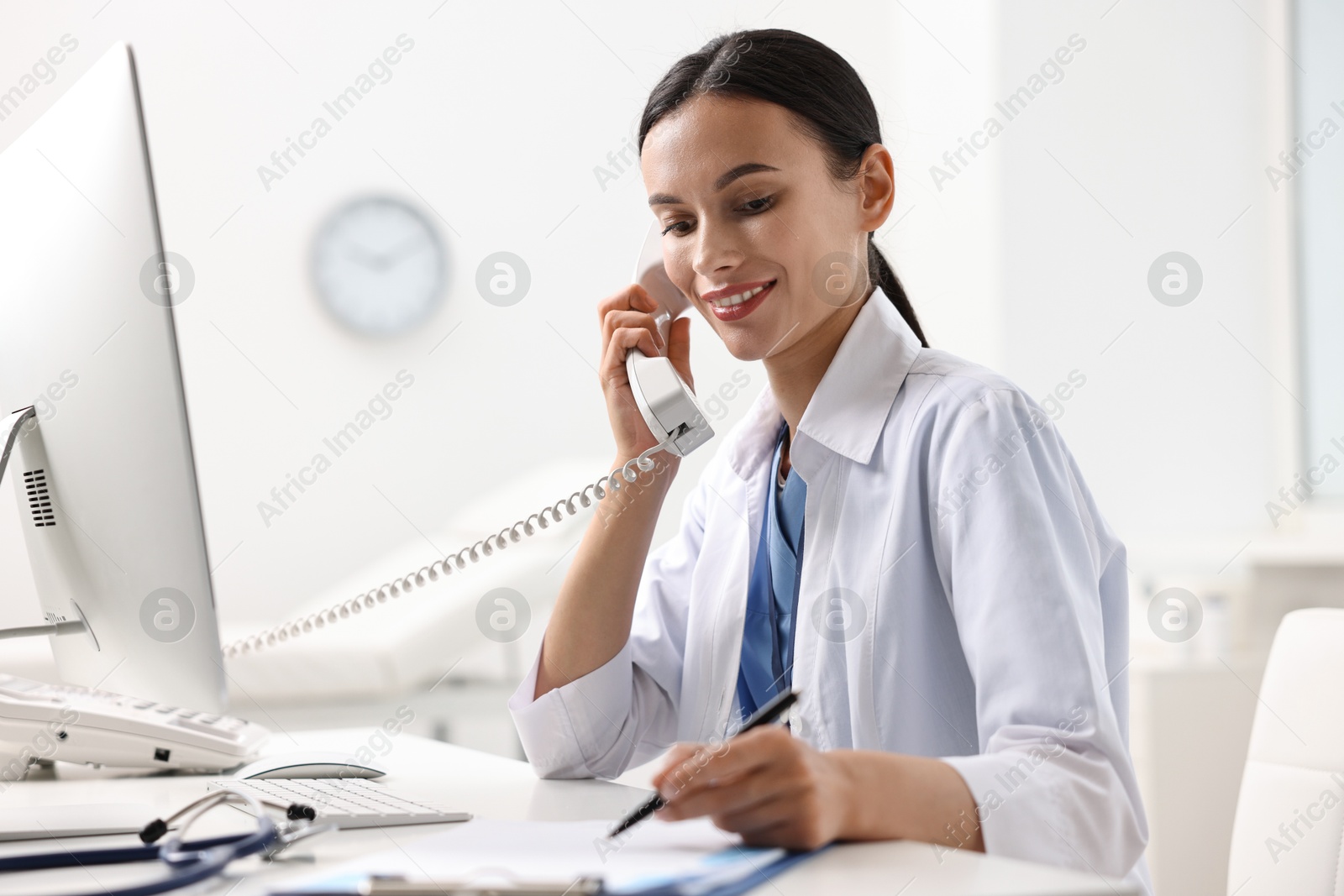 Photo of Smiling nurse consulting patient by phone at table in clinic