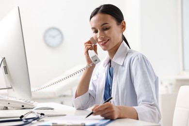 Photo of Smiling nurse consulting patient by phone at table in clinic