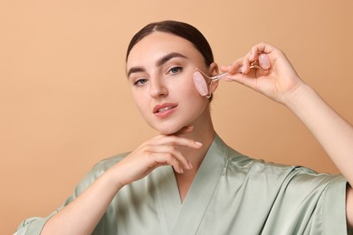 Photo of Beautiful young woman doing facial massage with roller on beige background