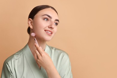 Photo of Beautiful young woman doing facial massage with roller on beige background, space for text