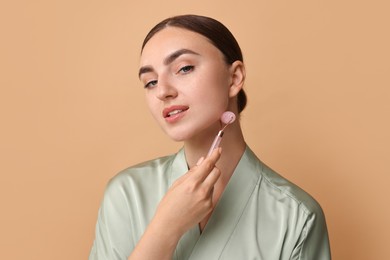 Beautiful young woman doing facial massage with roller on beige background