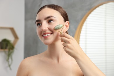 Beautiful young woman doing facial massage with roller indoors