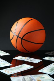 Photo of Basketball ball and dollar banknotes on black background