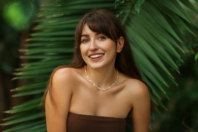 Portrait of smiling woman near palm leaves outdoors