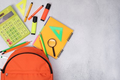 Photo of Flat lay composition with backpack and different school stationery on light grey table, space for text