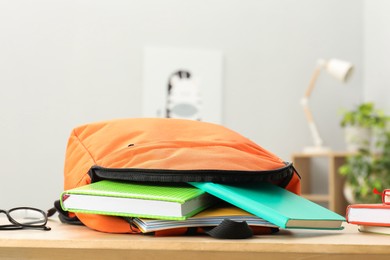 Photo of Backpack and different school stationery on wooden table indoors