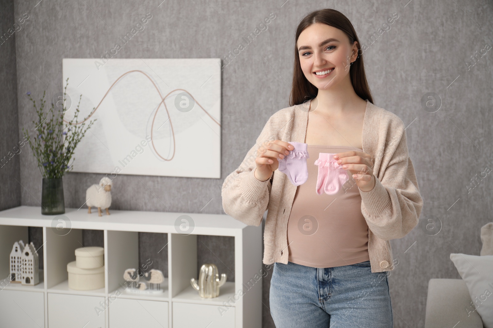 Photo of Expecting twins. Pregnant woman holding two pairs of socks at home, space for text