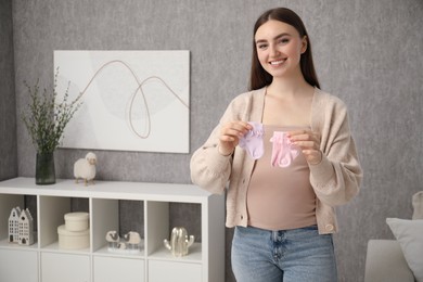 Expecting twins. Pregnant woman holding two pairs of socks at home, space for text