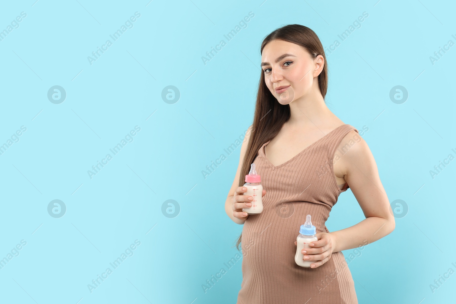 Photo of Expecting twins. Pregnant woman holding two bottles with milk on light blue background, space for text